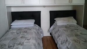 Una habitación con dos camas, cada una con cabeceros negros y ropa de cama estampada. Hay armarios blancos sobre las camas.