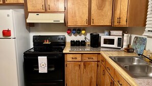 Una cocina con armarios de madera, una estufa negra, un refrigerador blanco, un microondas y un lavamanos de acero inoxidable.