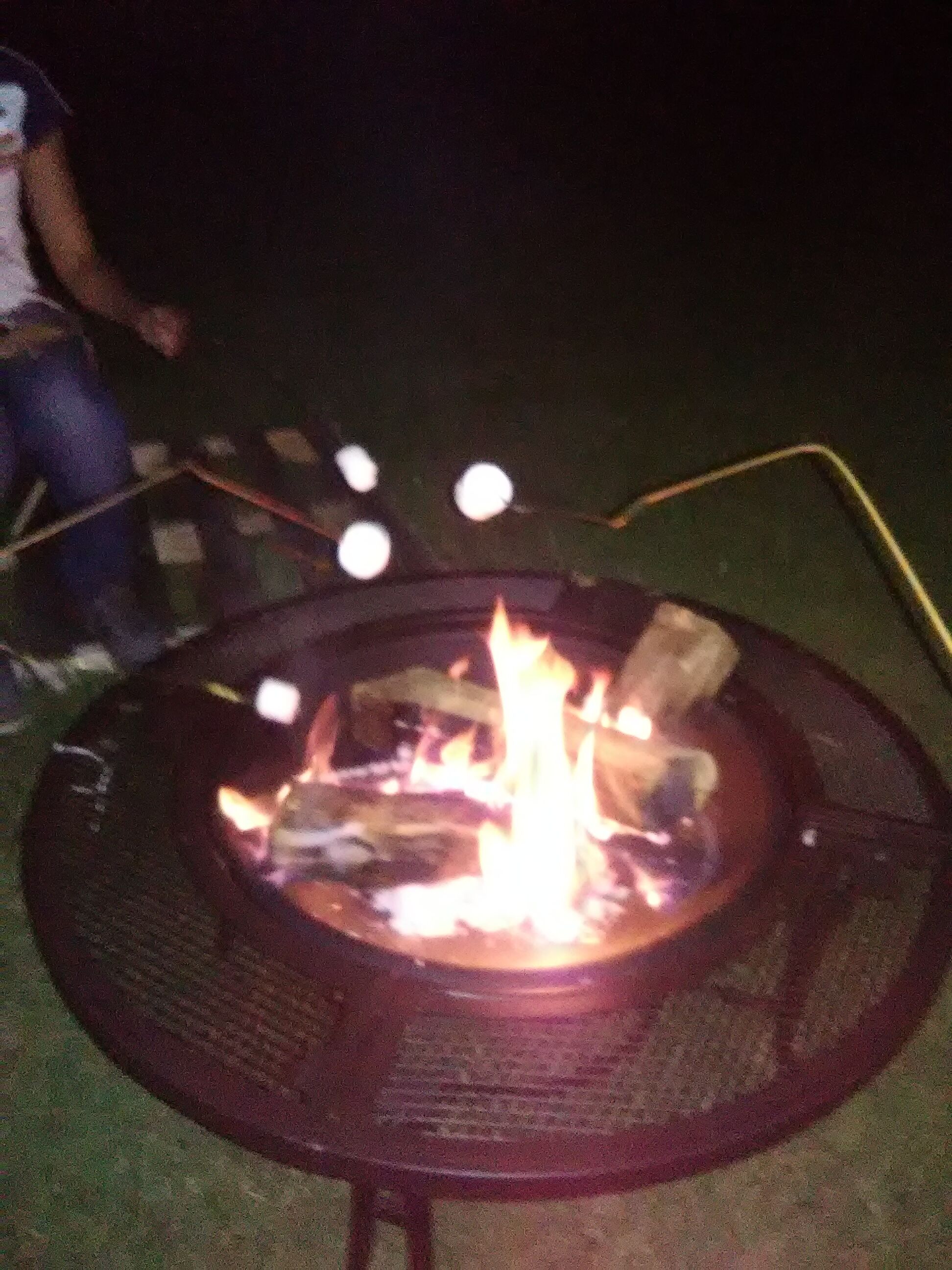A circular outdoor fire pit with flames, surrounded by a metal grate.