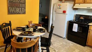Una cocina con una mesa de comedor lista para cuatro personas, armarios de madera, un refrigerador y una estufa.