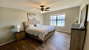 A bedroom with a wooden bed, a nightstand, a ceiling fan, a window, and a dresser. - Waterfront house with private dock and boat slip (Stigler)