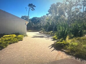 A paved pathway leading to a building with a white exterior, surrounded by greenery and trees. - Cozy Villa at Pebble Beach (Del Monte Forest)