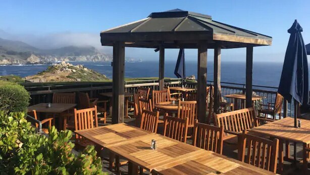 An outdoor seating area with wooden tables and chairs, a gazebo, and a view of the ocean.