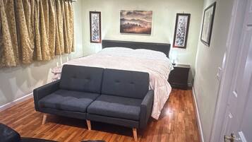 Une chambre à coucher avec un lit, un canapé, un plancher en bois et une porte.