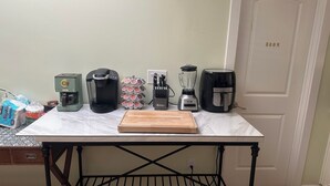 A kitchen counter with a coffee maker, a blender, a coffee machine, and a cutting board.