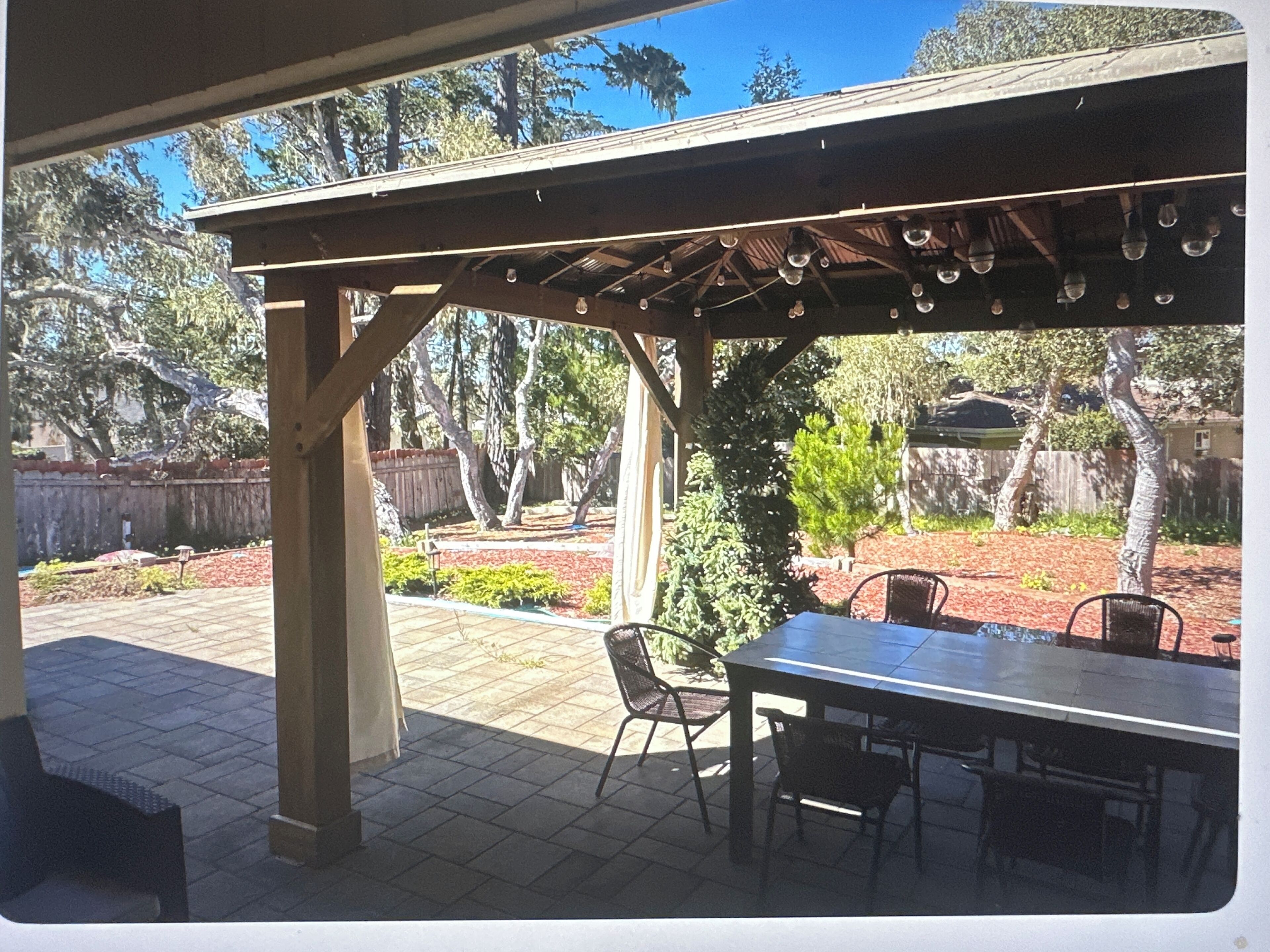 An outdoor patio with a covered seating area, a table, and chairs.