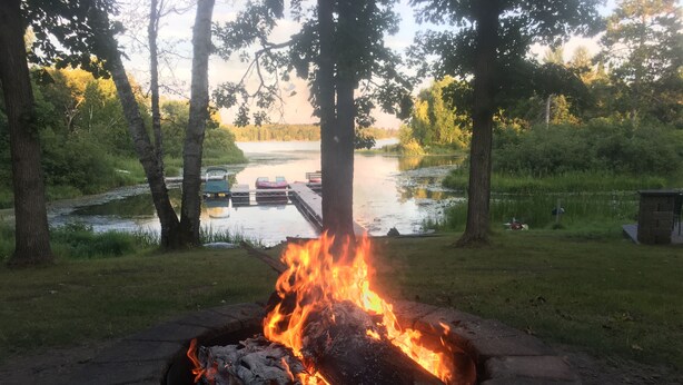 Un foyer extérieur aménagé dans un cadre naturel, avec un lac et un quai en arrière-plan.