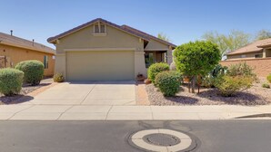 A single-story house with a garage, surrounded by small shrubs and a tree.