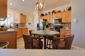 A kitchen with wooden cabinets, a dining table with chairs, a chandelier, and various kitchen appliances.