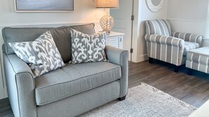 Una sala de estar con un sofá gris, un sillón a rayas y un espejo redondo en la pared.