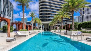 A swimming pool with lounge chairs and palm trees, surrounded by modern buildings. - ★LUXURIOUS★ King Suite Located at SLS Lux Brickell Building (Miami)