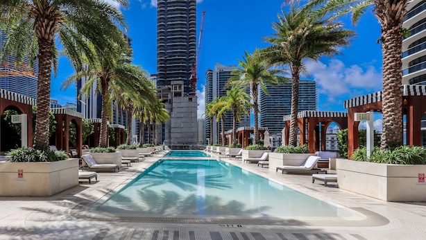 A pool area with lounge chairs, palm trees, and modern buildings in the background. - ★LUXURIOUS★ King Suite Located at SLS Lux Brickell Building (Miami)