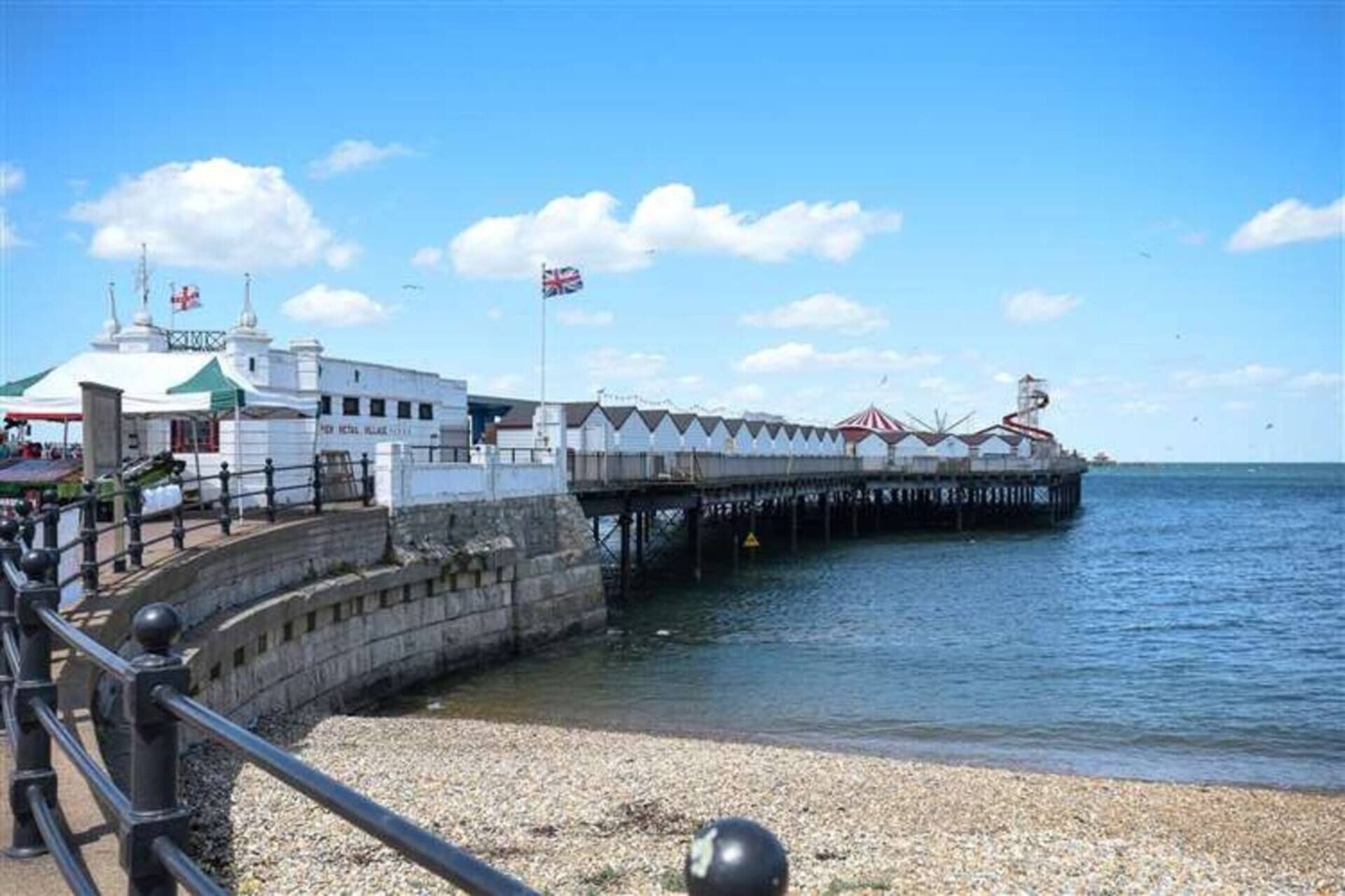 A pier extending into the water with a building at the end, featuring a flag and a lighthouse.
