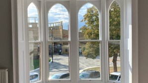 A bay window with multiple panes, offering a view of a parking area and surrounding buildings. - Elegant 2 Bed Georgian Apartment in Herne Bay (Herne Bay)