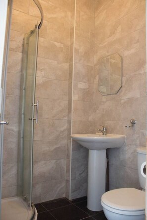 A bathroom with a glass shower enclosure, a pedestal sink, and a toilet.