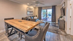 Un espace repas avec une table en bois et des chaises en métal, un ventilateur de plafond et une vue sur l’extérieur, accessible par une porte vitrée.