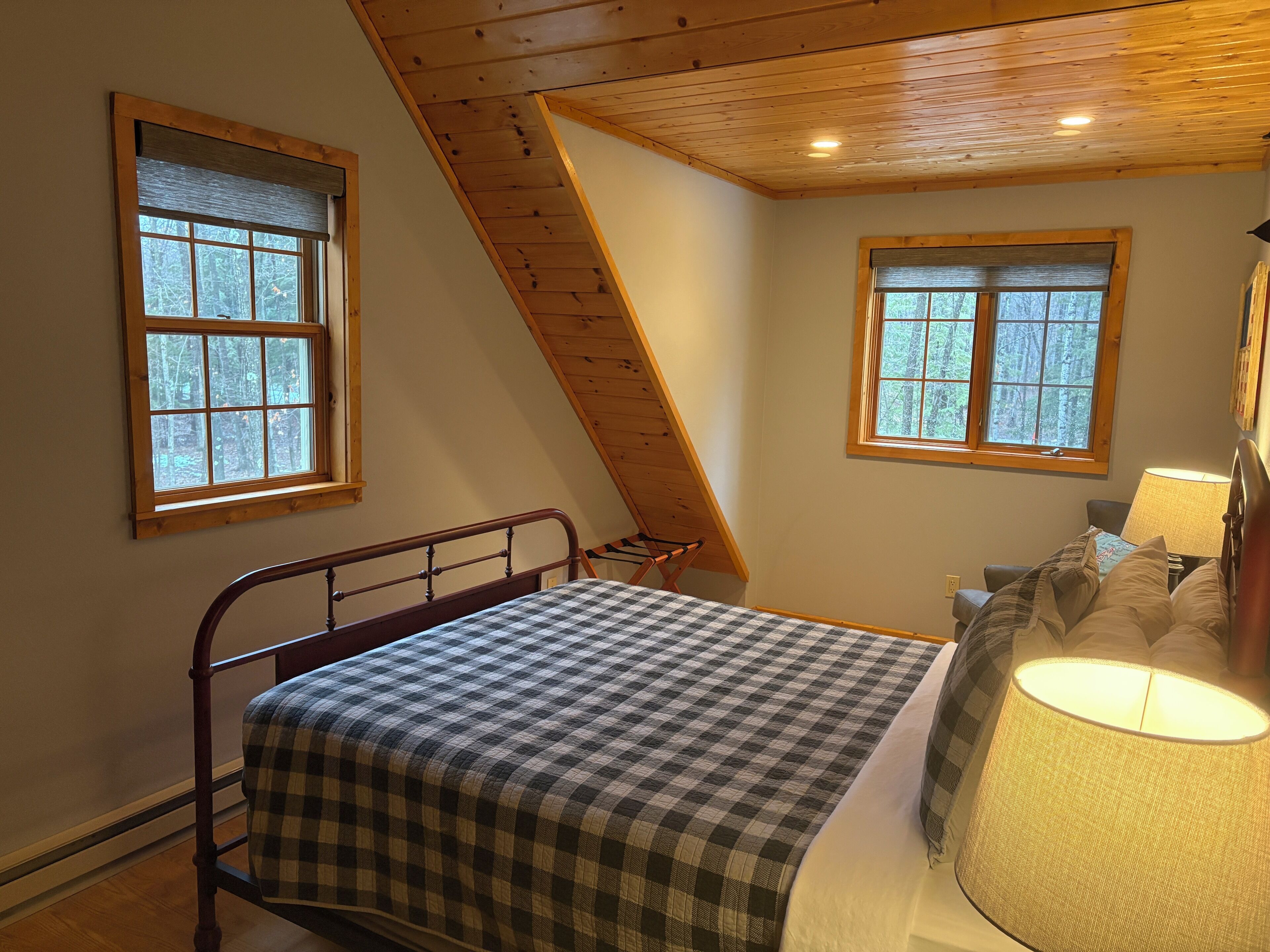 A bedroom with a bed, two windows, a sloped ceiling, and a nightstand with a lamp.
