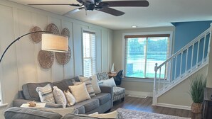 A living room with a gray sectional sofa, a ceiling fan, and a large window with blinds. - Water Front Home: Fisherman's' dream with private dock and beautiful sunsets (Brownstown Charter Township)