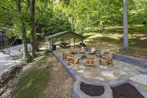 Uma área de estar coberta ao ar livre, com cadeiras Adirondack e uma mesa de piquenique, cercada por uma borda de pedra e um deck de madeira.