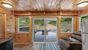 Et interiør af en træhytte med en skydedør af glas, der fører til en udendørs patio.