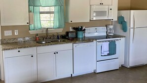 A compact kitchen with white cabinets, a microwave, a toaster, and a refrigerator. - Hunter's Ridge Cabins - 1 (Concan)