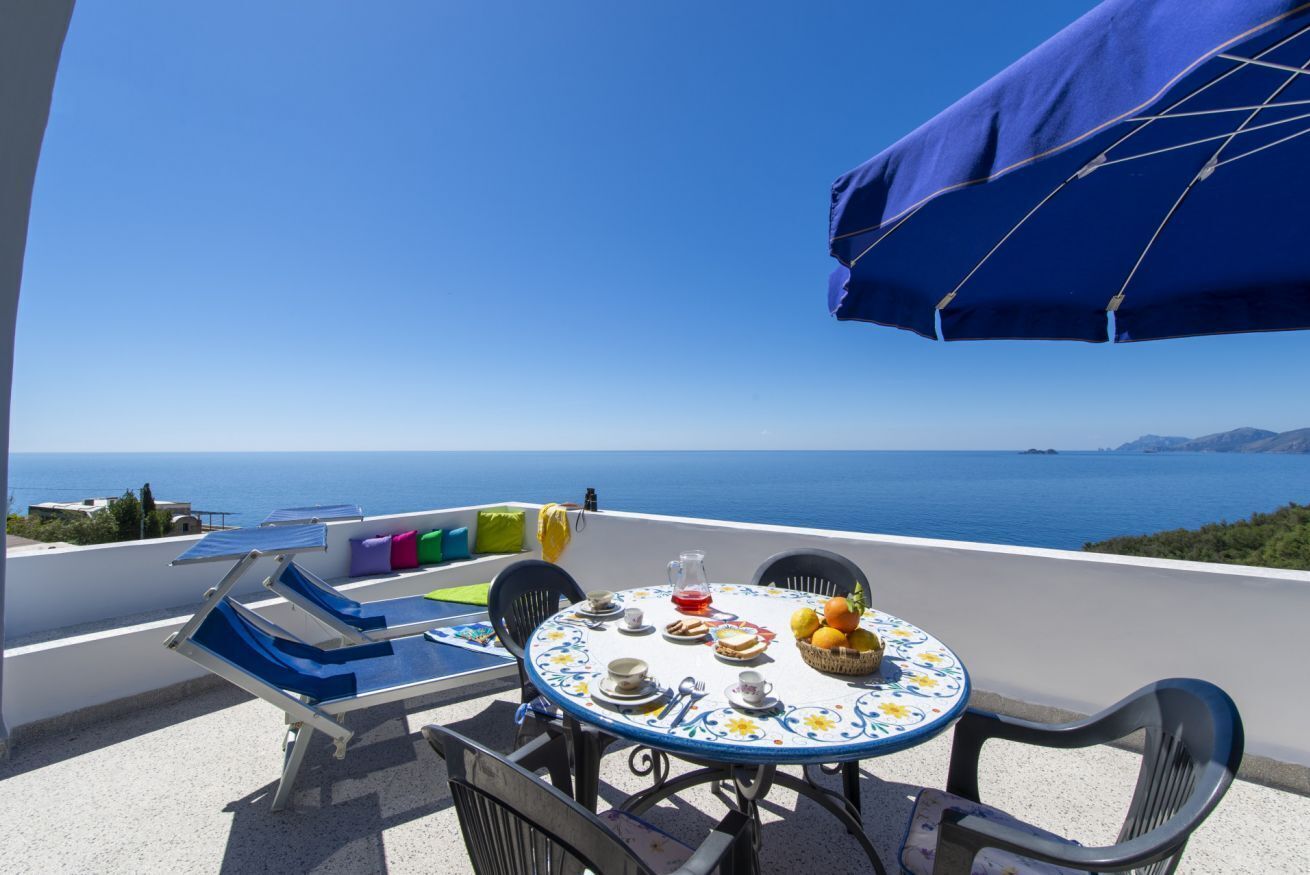 A terrace with a table set for two, overlooking a scenic coastal view.