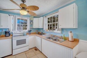 Kitchen features an oven, sink, and coffee maker, with a ceiling fan and two windows.