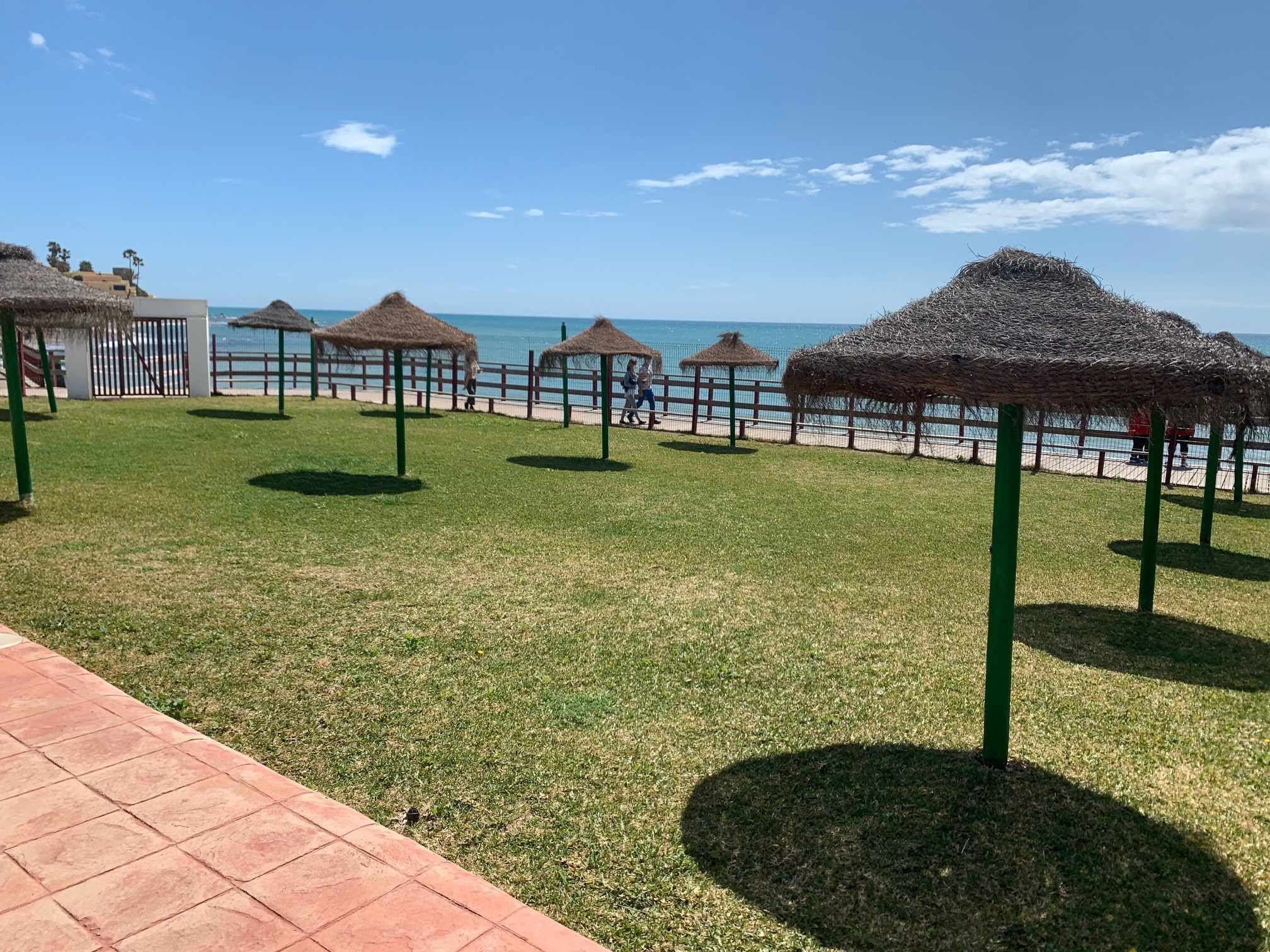 Eine Rasenfläche mit winkligen Dächern, einem Zaun und Blick aufs Meer.