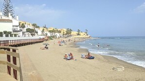 Une plage avec une promenade en bois, des gens qui se détendent et des bâtiments en arrière-plan.