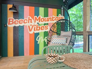 Un mur coloré sur lequel on peut lire le texte « Beech Mountain Vibes », et une chaise suspendue agrémentée de coussins.
