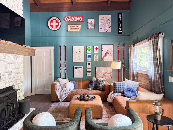 A cozy cabin interior with a fireplace, leather sofas, skis, and ski patrol signs.