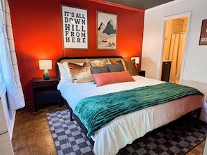 A bedroom with a bed, pillows, a nightstand, a lamp, a rug, and two wall art pieces.