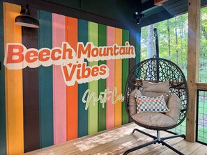 Une pièce avec un mur rayé aux couleurs vives, un fauteuil suspendu et une table en bois.