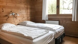 Ein Zimmer mit zwei Betten, Holzwänden, einem Fenster mit Vorhängen und einer Heizung.