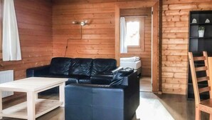 Ein gemütliches Blockhaushaus-Interieur mit einem schwarzen Ledersofa, einem Holztisch und einer Leiter zu einem Schlafbereich auf dem Dachboden.