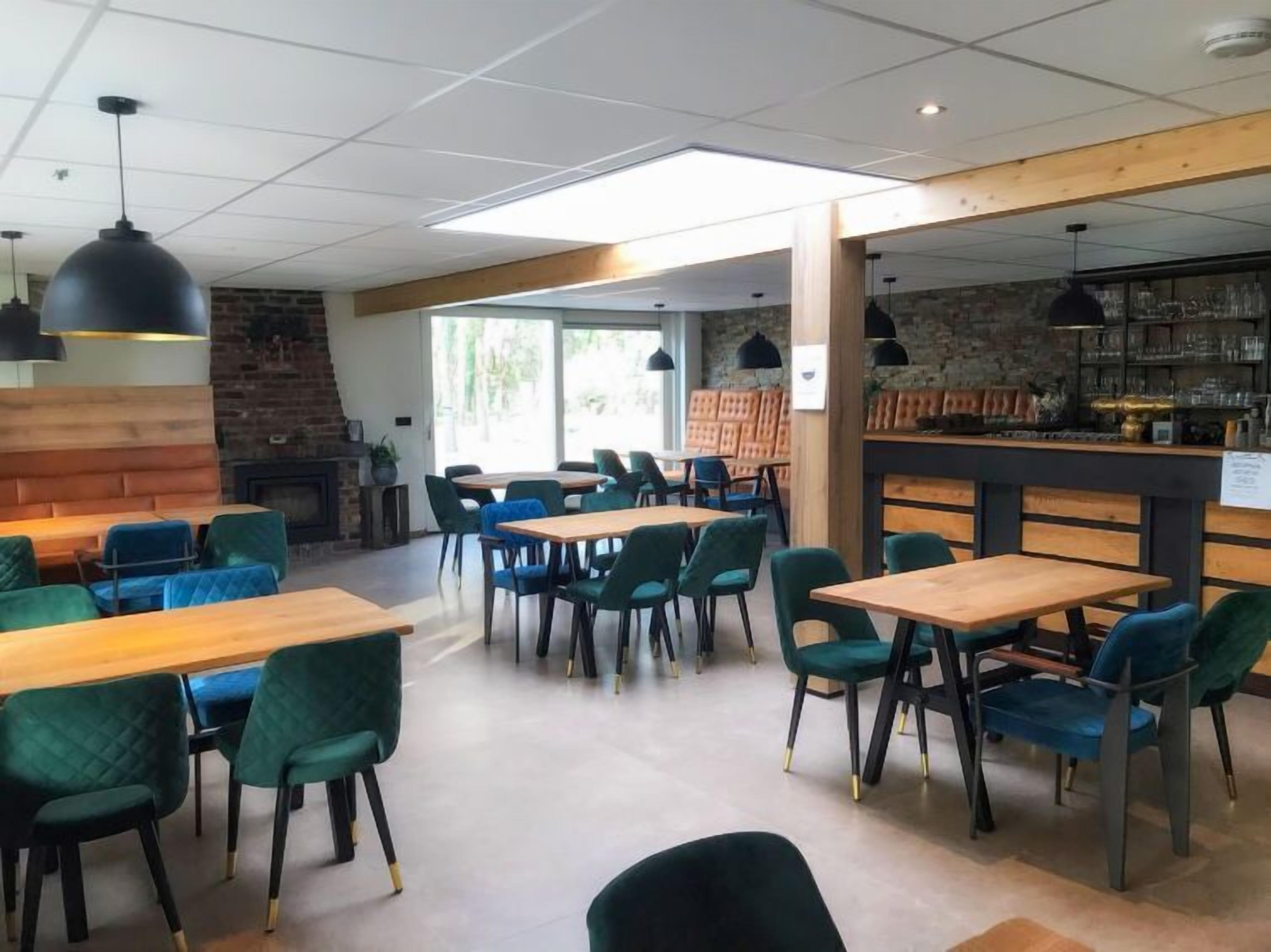 Un restaurant moderne avec des tables en bois et des chaises vertes, un mur en briques et un coin bar.