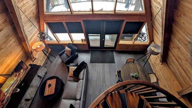 Innenansicht einer Holzhütte mit einem großen Oberlicht, einer Couch, einem Esstisch und einer Treppe.