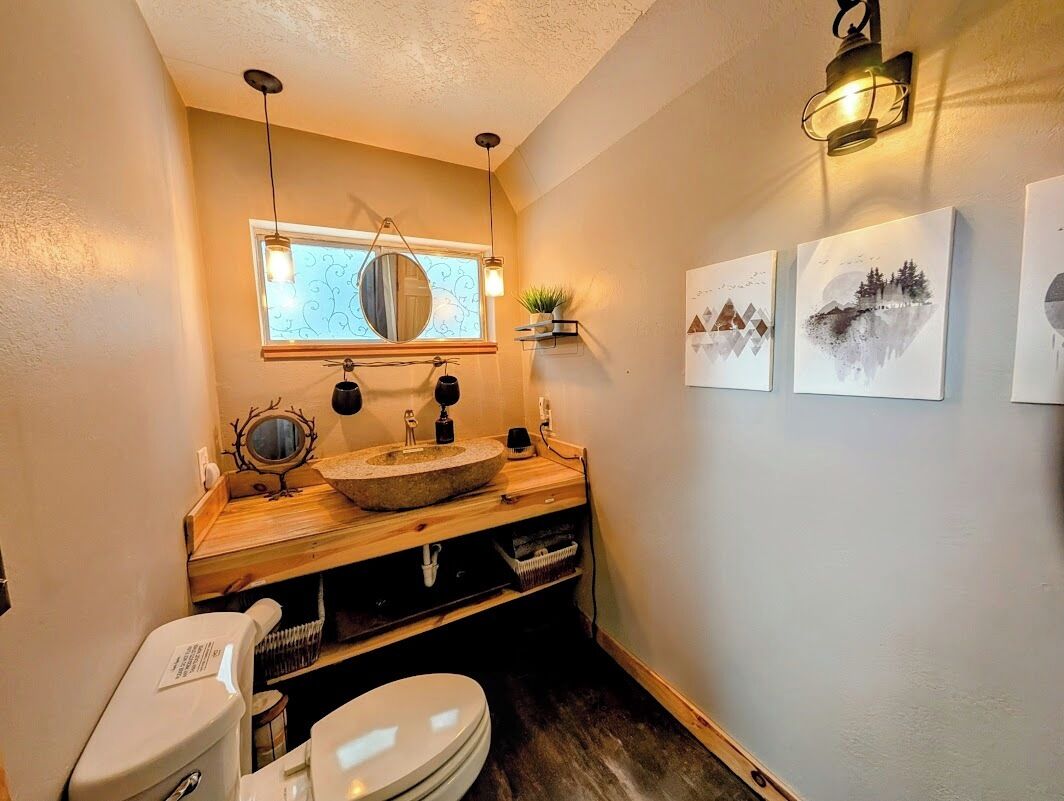 Une petite salle de bain avec un meuble-lavabo en bois, un lavabo rond, des toilettes et une fenêtre avec un miroir.