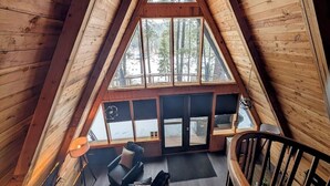 Ein gemütliches Holzhaus mit einem Giebeldach, einer Sitzecke mit Sofa und Sesseln und großen Fenstern mit Blick auf den umliegenden Wald.