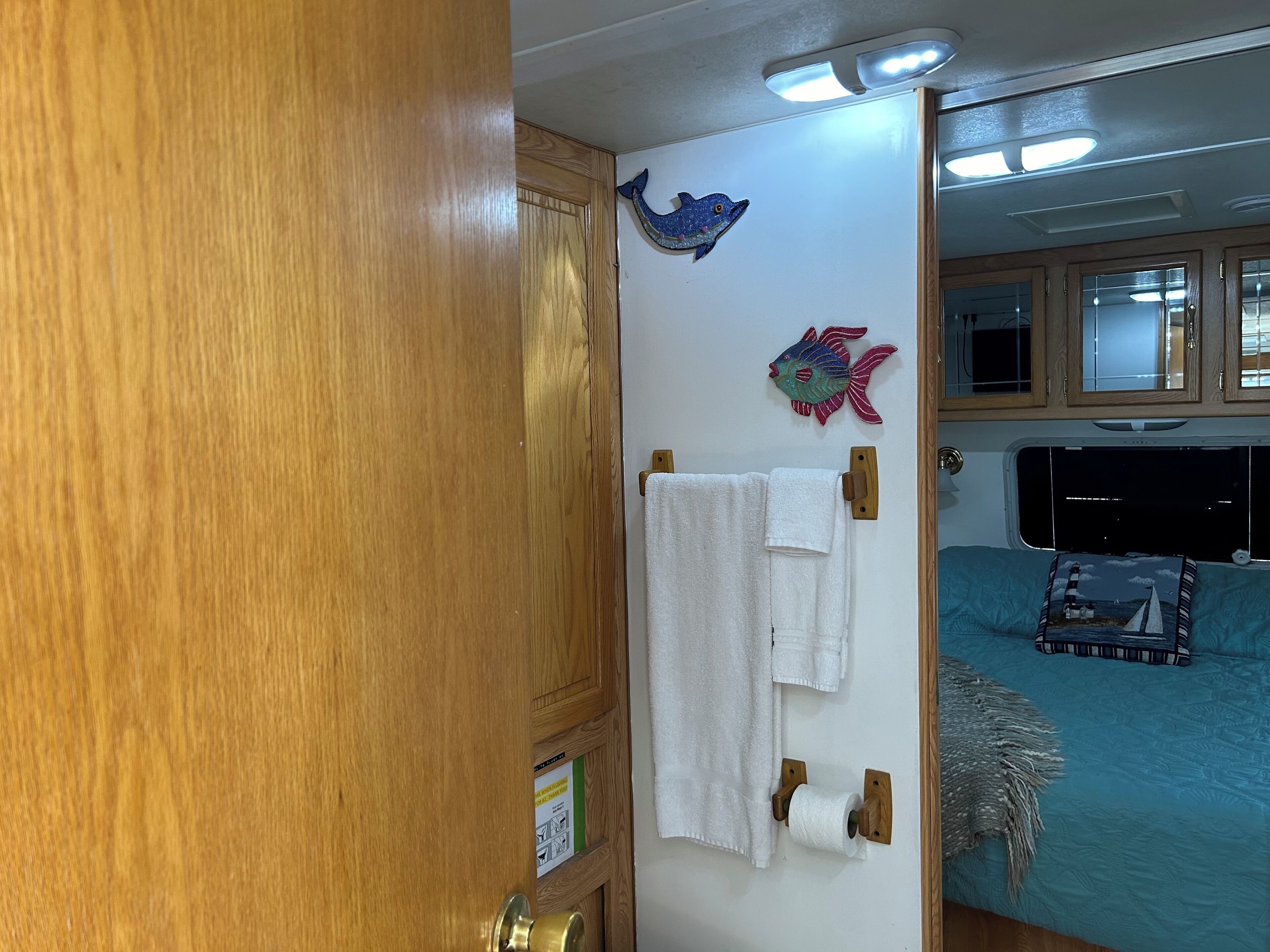 Un baño con armarios de madera, un perchero con toallas blancas y decoración de peces en la pared.