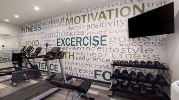A gym with cardio equipment, dumbbells, and motivational words on the wall.