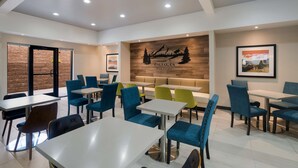 Un espace repas moderne avec plusieurs tables et chaises, un mur en bois orné d’une pancarte de bienvenue et un mur en briques avec une porte.