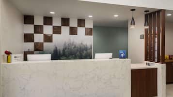 Un comptoir d’accueil au motif de marbre, un mur décoré de motifs à carreaux et une fresque représentant une forêt.