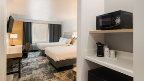 Une chambre d’hôtel avec deux lits, un bureau avec une chaise, une télévision, un four à micro-ondes et une machine à café.