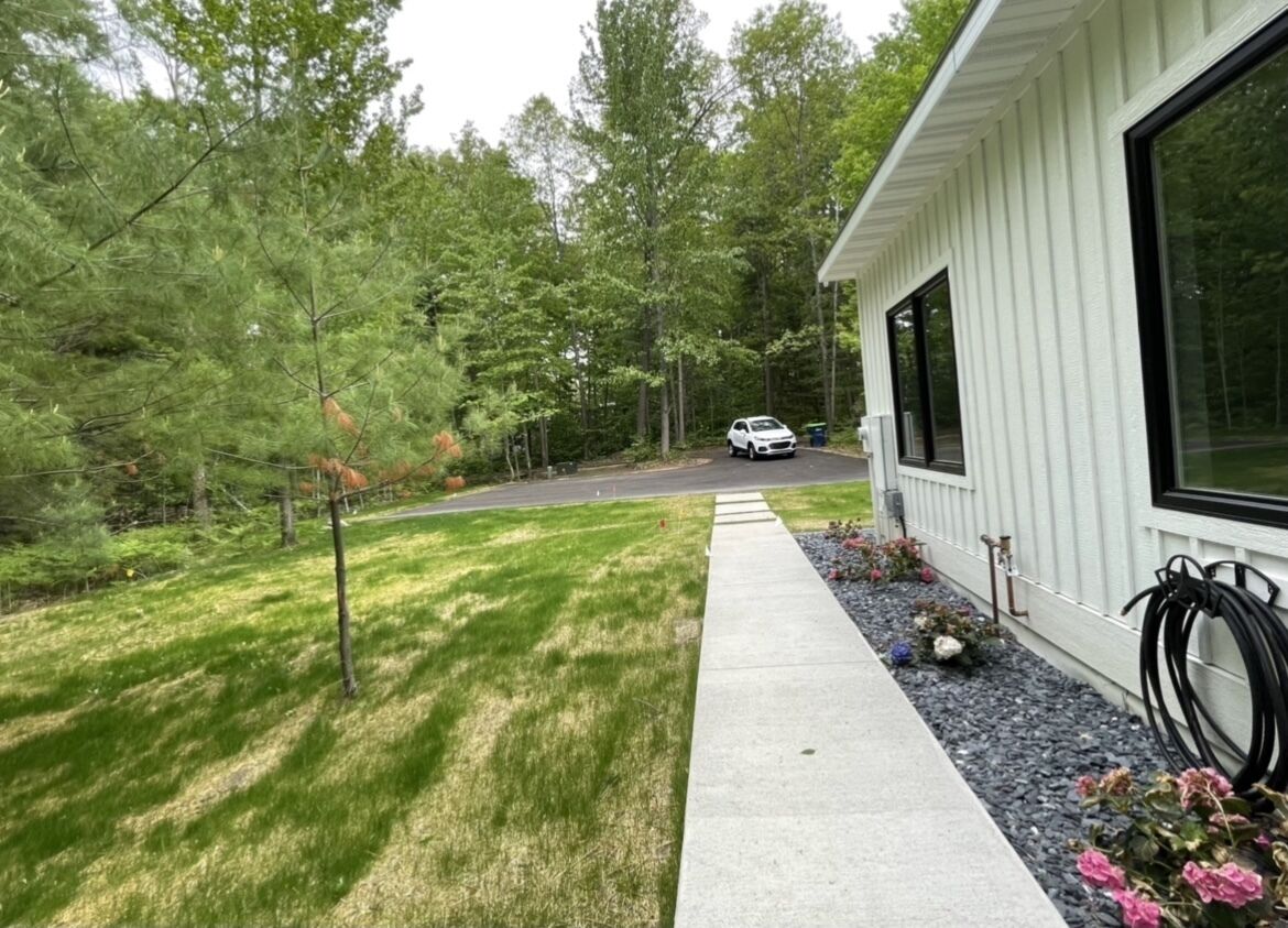 A residential property with a paved driveway leading to a garage, surrounded by a well-maintained lawn and trees.