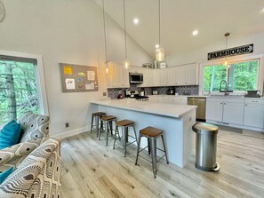 A modern kitchen with a central island, bar stools, and a 'Farmhouse' sign.