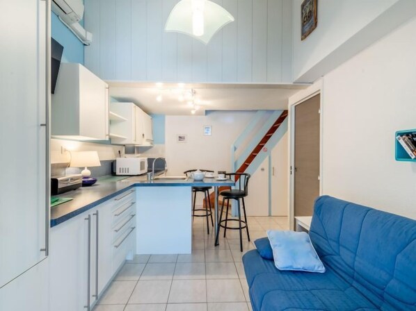 Cocina compacta con una isla central, comedor y un sofá azul.