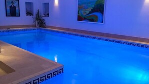 A swimming pool with blue lighting, a framed portrait, and a landscape painting on the wall.