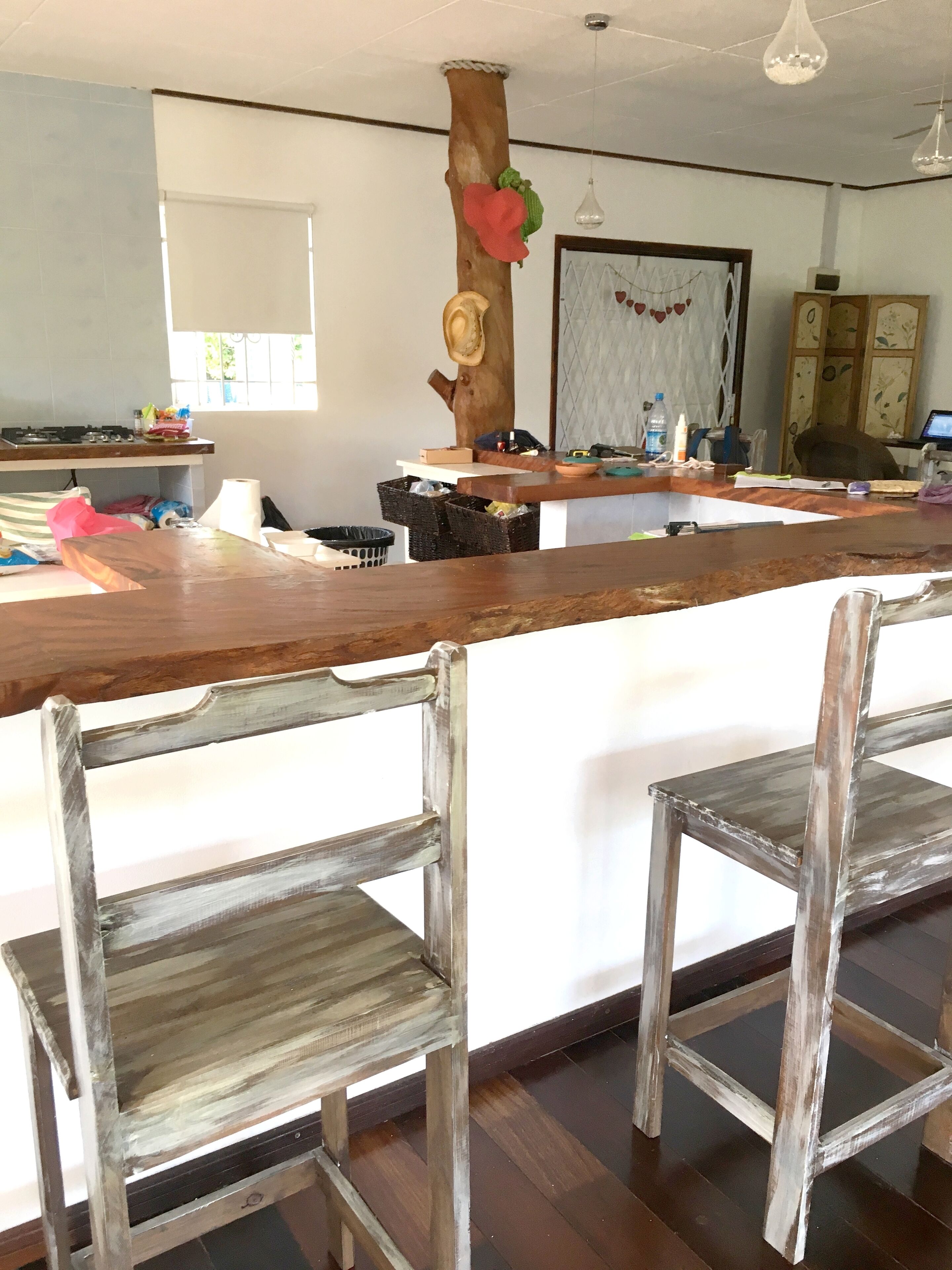 Une cuisine avec un îlot central en bois, deux chaises rustiques, une fenêtre à barreaux et une porte décorée d’un motif en forme de cœur.