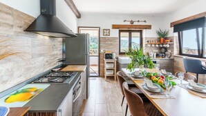 A modern kitchen with a gas stove, black range hood, and a dining area with a table set for two. - Villa for 4 with feature pool & great reviews (Bedar)